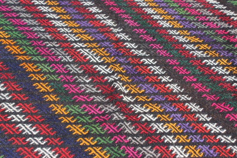 May include: A close-up of a colorful woven rug with a geometric pattern. The rug is made of wool and has a variety of colors, including red, green, blue, yellow, and white.