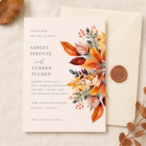 May include: A cream-colored wedding invitation card featuring watercolor autumn leaves in shades of orange, red, and gold on the right side. The text reads: Together with their families, Ashley Sprouse and Tanner Fulmer, joyfully invite you to their wedding celebration, Saturday, October 14th, two thousand twenty-year, The Harpeth Hotel, Franklin, Tennessee, dinner and dancing to follow.