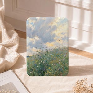 May include: A rectangular art print featuring an impressionistic painting of a lush meadow filled with small blue, yellow, and white wildflowers under a vast, cloudy sky with soft shades of blue, cream, and pale yellow brushstrokes throughout.