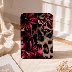 Puede incluir: Una funda rectangular para tableta con un estampado vibrante de lirios de color burdeos intenso con gotas de agua visibles en los pétalos, que contrasta con un patrón de estampado animal de leopardo beige y negro en el resto.