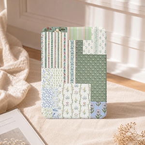 Könnte beinhalten: Eine rechteckige Tablethülle mit einem Patchwork-Design aus verschiedenen Blumen- und Streifenmustern in Salbeigrün, Hellblau, Creme und zartem Rosa. Die Oberfläche zeigt mehrere vertikale und horizontale Abschnitte mit botanischen Motiven.