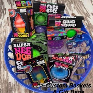 May include: A blue plastic basket filled with various Nee Doh sensory toys in their original packaging, including Teenie Nee Doh Fuzz Ball, Quad Squad, Super Nee Doh, Nice Cream Cones, Nice Sicle, and Nee Doh Dohnut, with text Custom Baskets & Gift Bags.