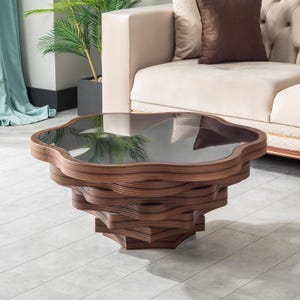 Puede incluir: Una mesa de centro con una base de madera de color marrón oscuro de varias capas con un diseño ondulado y apilado. La superficie superior es una pieza de vidrio oscuro y liso con forma de flor de pétalos redondeados que refleja el entorno.