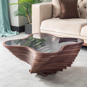 May include: A coffee table featuring a dark brown wooden base constructed from multiple stacked, curved layers that create a spiraling, organic shape. The top of the table is a smooth, reflective black glass surface with a distinct clover-like outline.
