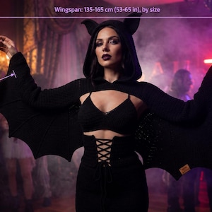 May include: A black knit bat-wing shrug featuring a hood with pointed ears, a cropped bodice, and scalloped wing edges. The garment has a wingspan of 135-165 cm and a sleeve length of 58-64 cm, available in finished sizes S-XL.