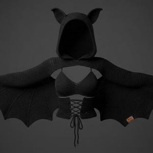 May include: A black crocheted garment set featuring a hooded shrug with bat-wing sleeves and pointed ears. The set includes a matching bralette and a corset-style bodice with front lace-up detailing and hanging ties, all crafted in a solid black knit.