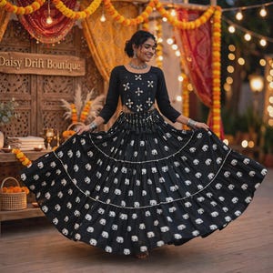 May include: A black long-sleeved top and a matching floor-length skirt featuring a repeating white elephant pattern. The top has a round neckline with silver-toned embellishments. The skirt is pleated with horizontal silver-toned trim accents.