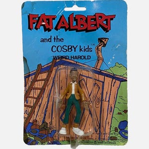 以下が含まれることがあります： 「Fat Albert and the Cosby Kids」のウィアード・ハロルドのアクションフィギュア。オリジナルのブリスターパック入り。フィギュアはタンカラーのジャケット、白いシャツ、緑のズボン、白い靴を着用。台紙には木造小屋のイラストが描かれている。