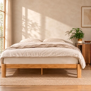 May include: A light-toned wooden bed frame with four sturdy legs supporting a white mattress. The bed is dressed in a textured beige duvet cover and two matching pillows, creating a neutral and clean appearance for this bedroom furniture piece.