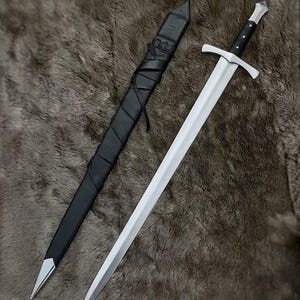 May include: A double-edged steel sword with a silver-toned crossguard and a black grip featuring three silver rivets. The sword is accompanied by a black scabbard wrapped in black leather strips, finished with a silver-toned metal tip at the end.
