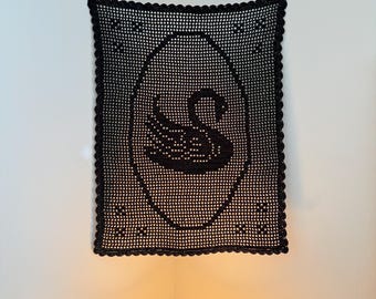 May include: A rectangular black crochet wall hanging featuring a central oval frame containing a silhouette of a swan. The piece is crafted with a grid-like pattern and finished with a scalloped border along all four edges of the textile.
