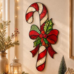 May include: A stained glass candy cane wall decoration featuring alternating red and white textured glass segments. A large red bow with green holly leaves and red berries is attached to the center of the candy cane, all outlined in black metal.