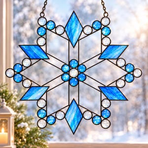 May include: A snowflake-shaped stained glass suncatcher featuring a central cluster of blue and clear circular glass pieces, surrounded by six elongated blue diamond-shaped glass panels and additional clear circular glass accents in a metal frame.
