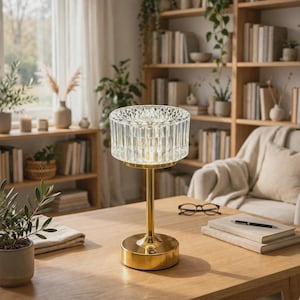 Puede incluir: Una lámpara de mesa con una pantalla cilíndrica de cristal transparente facetado y una base de metal dorado pulido. La lámpara cuenta con un tallo delgado y una base circular, con el texto ZVCRAFTS visible en la esquina superior derecha.