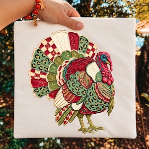Peut inclure: Un carré de tissu blanc orné d'une illustration texturée et multicolore de dinde. La dinde présente une queue en éventail vibrante avec des sections rouges, vertes et crème, intégrant des motifs léopard, à carreaux et des paillettes dorées.