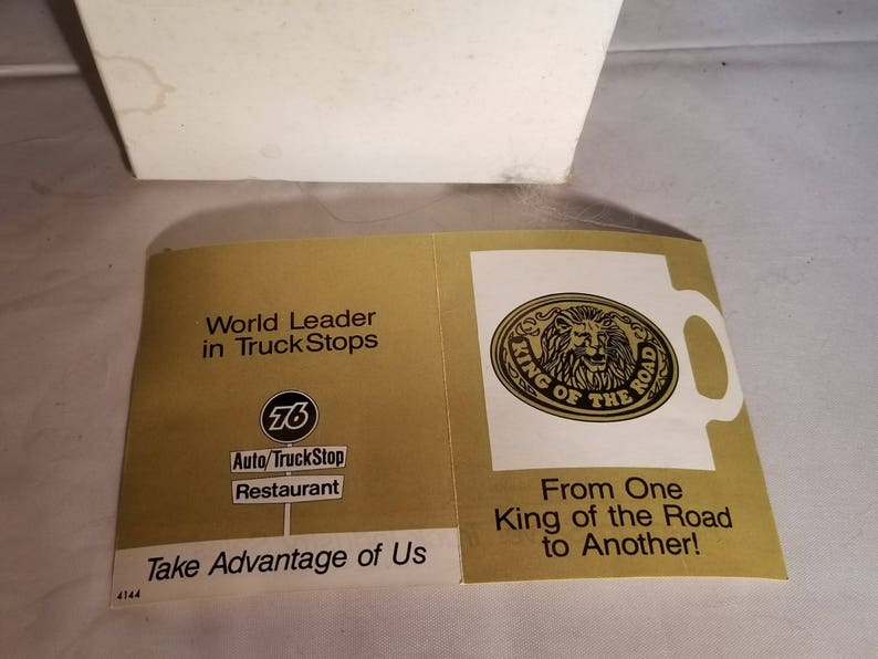 May include: A gold and white advertisement for a truck stop chain called "76 Auto/TruckStop Restaurant". The ad features a lion logo with the text "King of the Road" and the slogan "From One King of the Road to Another!"