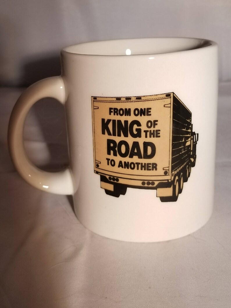 May include: White ceramic coffee mug with a black and brown illustration of a semi-truck. The text on the truck reads "From one King of the Road to another."