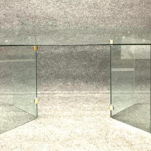 May include: A clear glass table with a rectangular top and a simple, modern design. The table has a glass base with four legs.