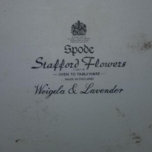 May include: A white ceramic plate with a black and white logo that reads "Spode Stafford Flowers - Oven to Tableware - Made in England Weigela & Lavender".