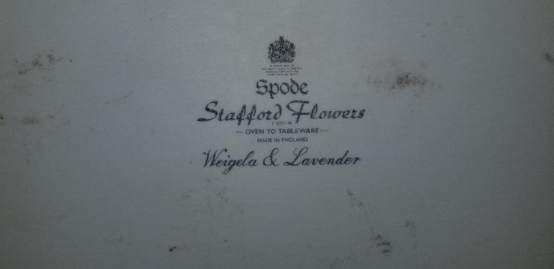May include: A white ceramic plate with a black and white logo that reads "Spode Stafford Flowers - Oven to Tableware - Made in England Weigela & Lavender".