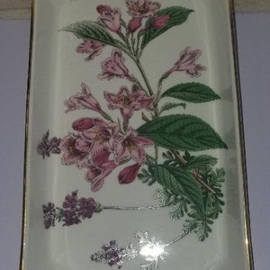 May include: A white rectangular ceramic dish with a gold rim features a floral design of pink flowers and green leaves.