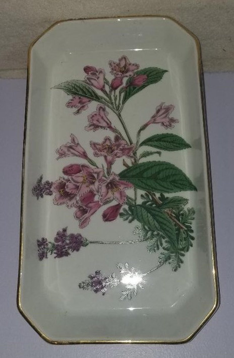 May include: A white rectangular ceramic dish with a gold rim features a floral design of pink flowers and green leaves.