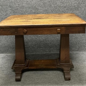 May include: A rectangular wooden table with a medium brown finish, featuring a flat top surface, a single horizontal drawer with two small square knobs, and two sturdy vertical legs connected by a low horizontal support beam.