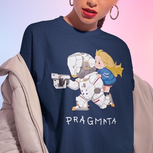 May include: A navy blue t-shirt featuring a graphic illustration of a white armored astronaut figure carrying a small blonde character on their back, with the text PRAGMATA printed in white below the figures on the front of the garment.
