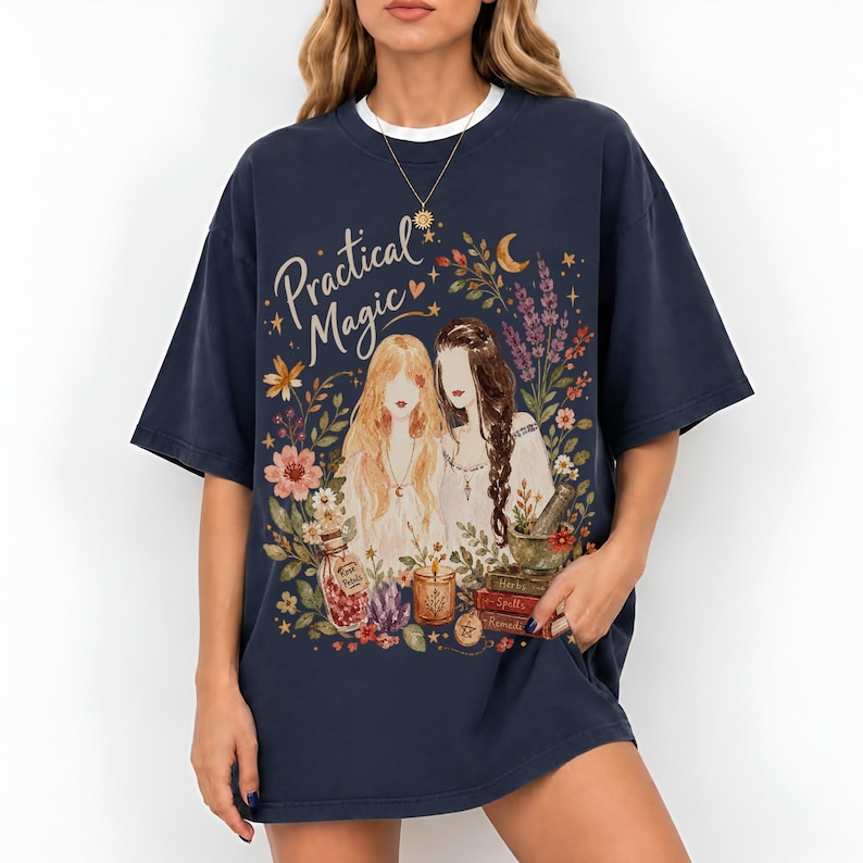 May include: A dark navy blue short-sleeve t-shirt featuring a graphic print with the text "Practical Magic" above two figures surrounded by flowers, a crescent moon, a jar labeled "Rose Petals," a candle, and a stack of books labeled "Spells."