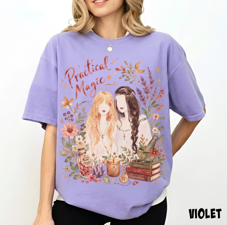 May include: A light purple t-shirt featuring a graphic illustration of two figures with long hair surrounded by flowers, a crescent moon, a jar labeled Rose Petals, a candle, a mortar and pestle, and a stack of books labeled Herbs, Spells, and Remedies.