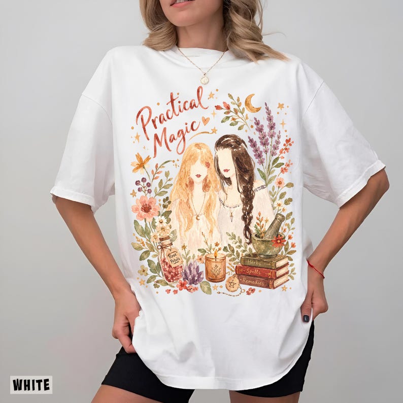 May include: A white short-sleeve t-shirt featuring a watercolor-style graphic with the text "Practical Magic". The design includes two figures surrounded by flowers, a bottle labeled "Rose Petals", a candle, a mortar and pestle, and stacked books.