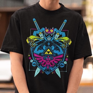 Peut inclure: Un t-shirt noir à manches courtes avec un imprimé graphique aux couleurs vives. Le motif présente un bouclier central avec une triforce jaune, entouré de deux épées, d'un masque stylisé et de divers motifs géométriques bleus, roses et jaunes.