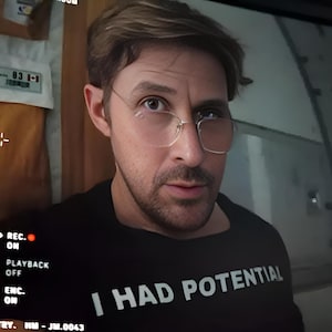 Könnte beinhalten: Eine Person mit kurzem braunem Haar und heller Brille trägt ein schwarzes T-Shirt mit dem weißen Text I HAD POTENTIAL auf der Vorderseite. Das Bild enthält eine digitale Aufnahmeoberfläche mit dem Text REC ON und PLAYBACK OFF.