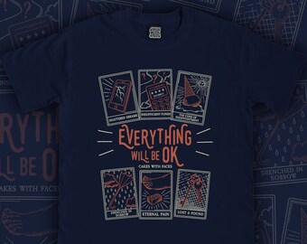 Könnte beinhalten: Ein marineblaues T-Shirt mit einem grafischen Design von Tarotkarten. Die Karten zeigen Illustrationen von einem kaputten Telefon, einem Taschenrechner mit einem Passwort, einem Eiswaffel, einem Regenschirm mit Regentropfen, einem Fuß mit einem Ziegelstein und einem Schlüssel. Der Text auf dem Shirt lautet "Everything will be ok" und "Cakes with faces".