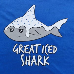 May include: A blue t-shirt with a cartoon illustration of a gray shark with white frosting and blue sprinkles. The text "Great Iced Shark" is printed below the shark.