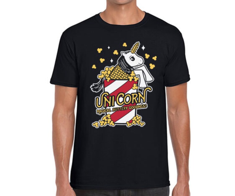 May include: Black t-shirt with a white unicorn in a red and white striped popcorn bucket. The text "Unicorn" is above the bucket and "Magical Buttery Goodness" is below the bucket.