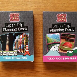 Op de afbeelding: Twee grijze kaartspellen met kleurrijke afbeeldingen en tekst. De bovenste kaart van elk spel heeft de tekst "Japan Trip Planning Deck". De linker kaart heeft een afbeelding van de Tokyo Tower en de tekst "TOKYO: ATTRACTIONS". De rechter kaart heeft een afbeelding van de Mount Fuji en de tekst "TOKYO: FOOD & DAY TRIPS".