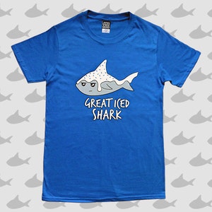 May include: A blue t-shirt with a cartoon illustration of a shark with white frosting and sprinkles. The text "Great Iced Shark" is printed below the shark.