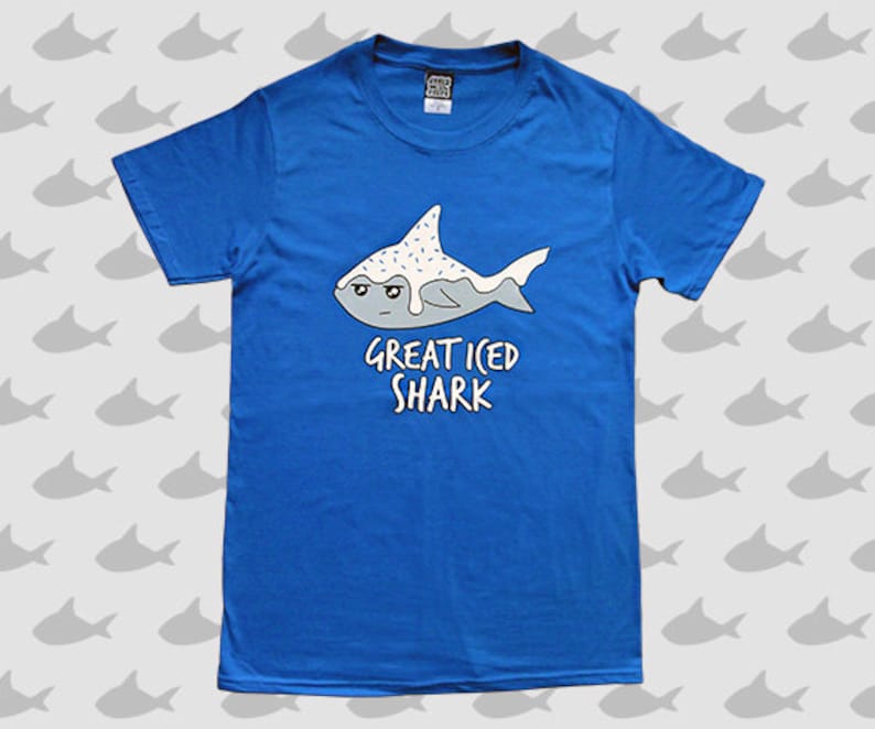 May include: A blue t-shirt with a cartoon illustration of a shark with white frosting and sprinkles. The text "Great Iced Shark" is printed below the shark.