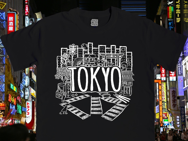 May include: Black t-shirt with a white graphic design of a cityscape with the word "TOKYO" in large letters. The design includes buildings, a street crossing, and other details.