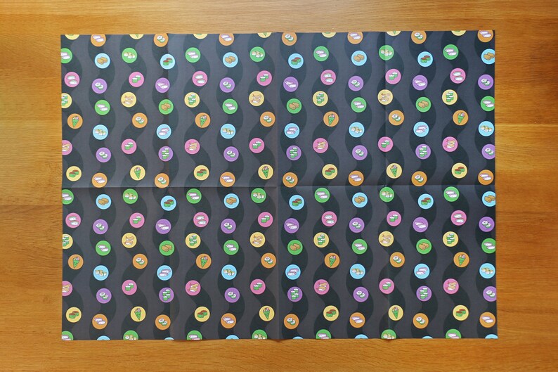 May include: A sheet of black wrapping paper with a repeating pattern of colourful sushi rolls. The sushi rolls are arranged in a wavy pattern.