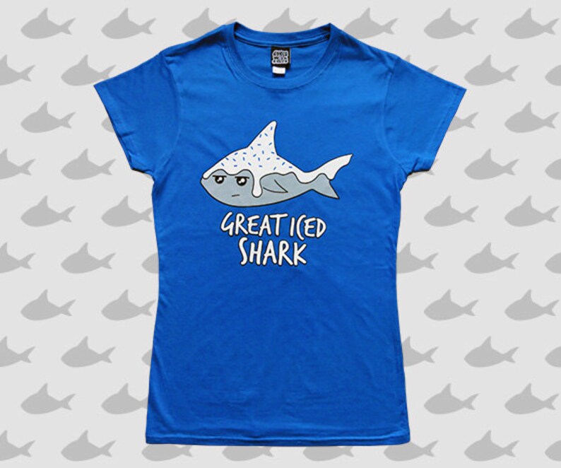 May include: A royal blue t-shirt with a white cartoon shark with blue icing and sprinkles. The text "Great Iced Shark" is printed below the shark.