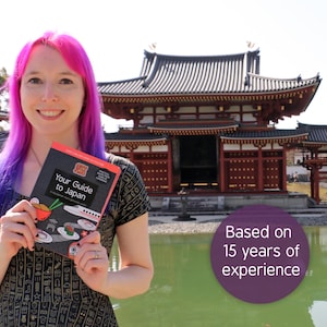 Pu&ograve; includere: Una persona con capelli rosa e viola tiene in mano una guida turistica intitolata "Your Guide to Japan" di fronte a un tradizionale edificio giapponese. La copertina presenta illustrazioni di cibo giapponese. Il testo sull'immagine recita "Based on 15 years of experience."