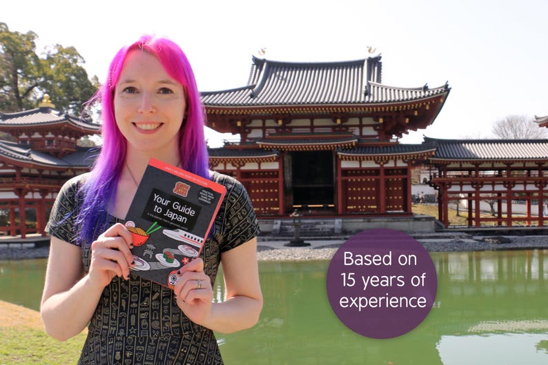 Pu&ograve; includere: Una persona con capelli rosa e viola tiene in mano una guida turistica intitolata "Your Guide to Japan" di fronte a un tradizionale edificio giapponese. La copertina presenta illustrazioni di cibo giapponese. Il testo sull'immagine recita "Based on 15 years of experience."