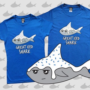 May include: Two blue t-shirts with a cartoon shark graphic. The shark is white with blue sprinkles and the text "Great Iced Shark".