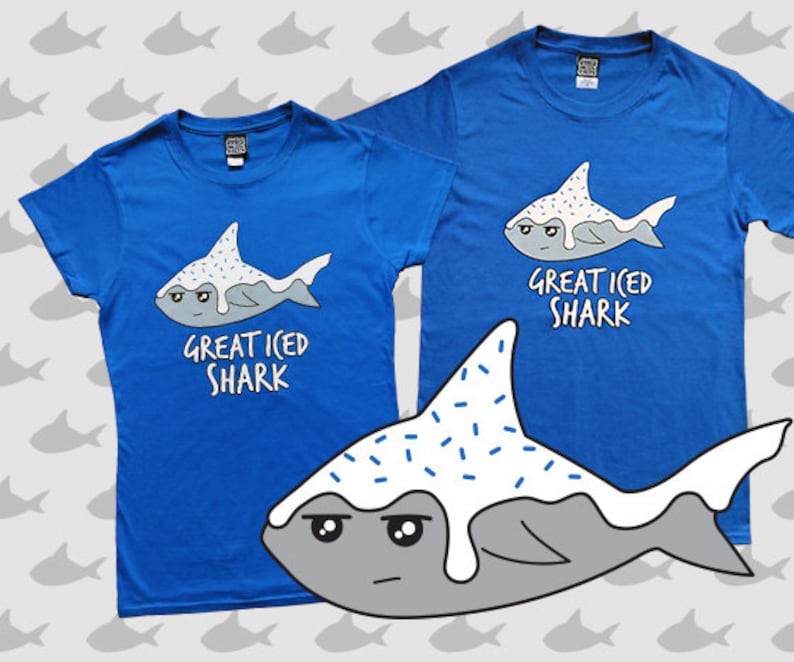May include: Two blue t-shirts with a cartoon shark graphic. The shark is white with blue sprinkles and the text "Great Iced Shark".