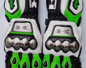 May include: A pair of black, white, and lime green motorcycle gloves featuring the Kawasaki logo and Ninja branding. The gloves include metallic knuckle protectors, reinforced finger padding, and the text D TEC ENGINEERED and SCP CONCEPT.