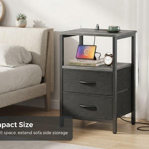 May include: A gray nightstand with a black metal frame, featuring an open top shelf and two fabric drawers with black handles. The top surface includes a built-in power outlet with a cord. The text Compact Size Fit small space, extend sofa side storage is visible.
