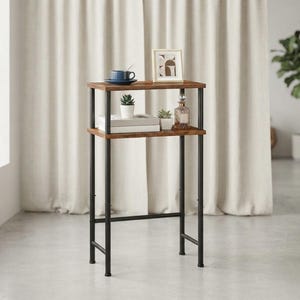 May include: A tall, narrow console table featuring two rectangular wooden shelves with a dark brown finish, supported by a black metal frame. The top shelf holds a blue cup, a small framed picture, and the bottom shelf holds two small potted plants.