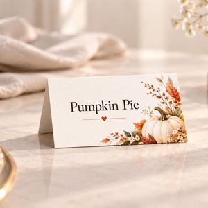 Może przedstawiać: Biała, składana wizytówka z napisem Pumpkin Pie czcionką szeryfową, ozdobiona małym czerwonym sercem oraz akwarelową ilustracją białej dyni otoczonej jesiennymi liśćmi, jagodami i suszonymi roślinami po prawej stronie.
